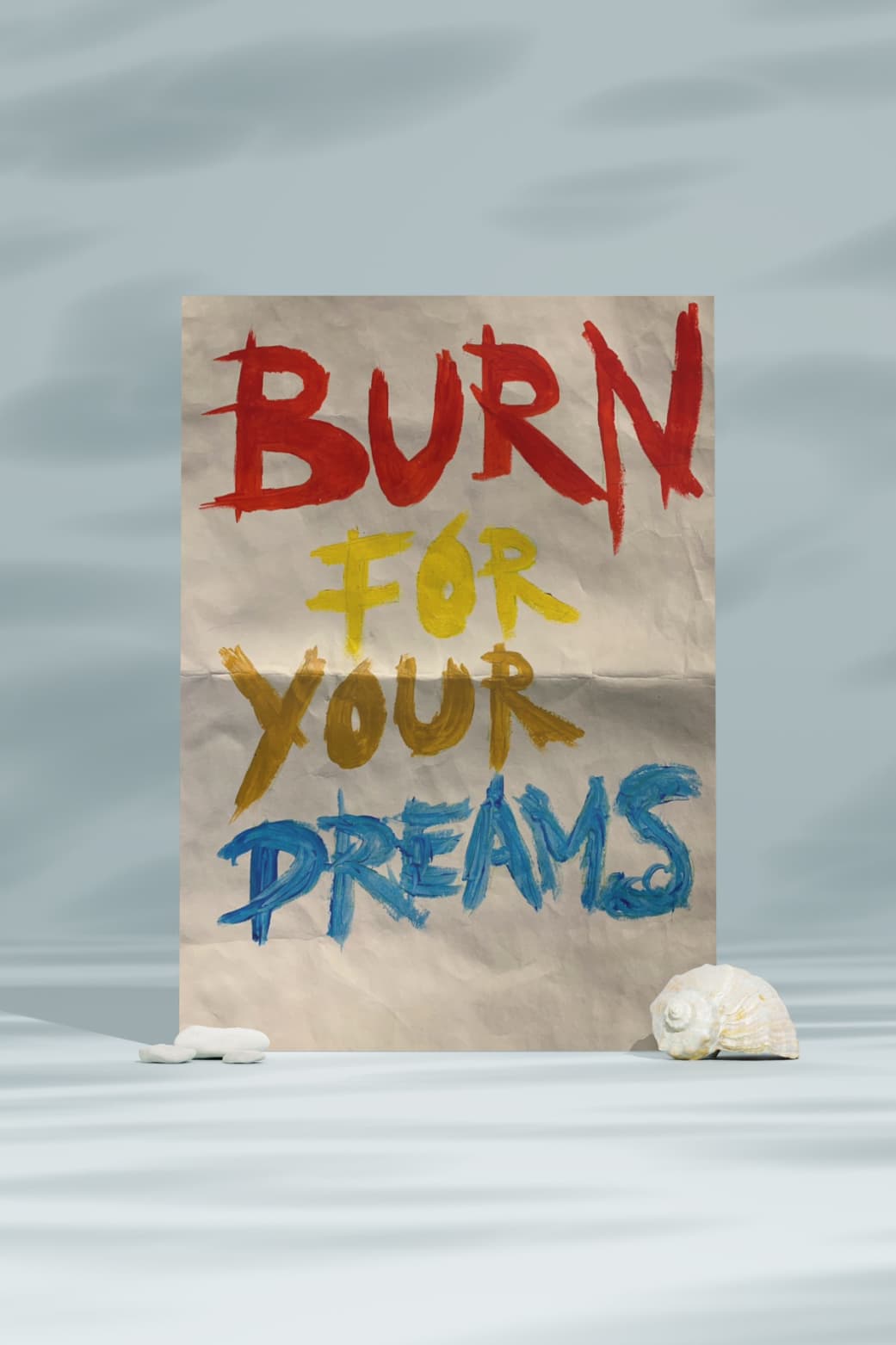 A poster with the words "BURN FOR YOUR DREAMS" written in bold, colorful letters on a crumpled piece of paper. The background is a light blue gradient.