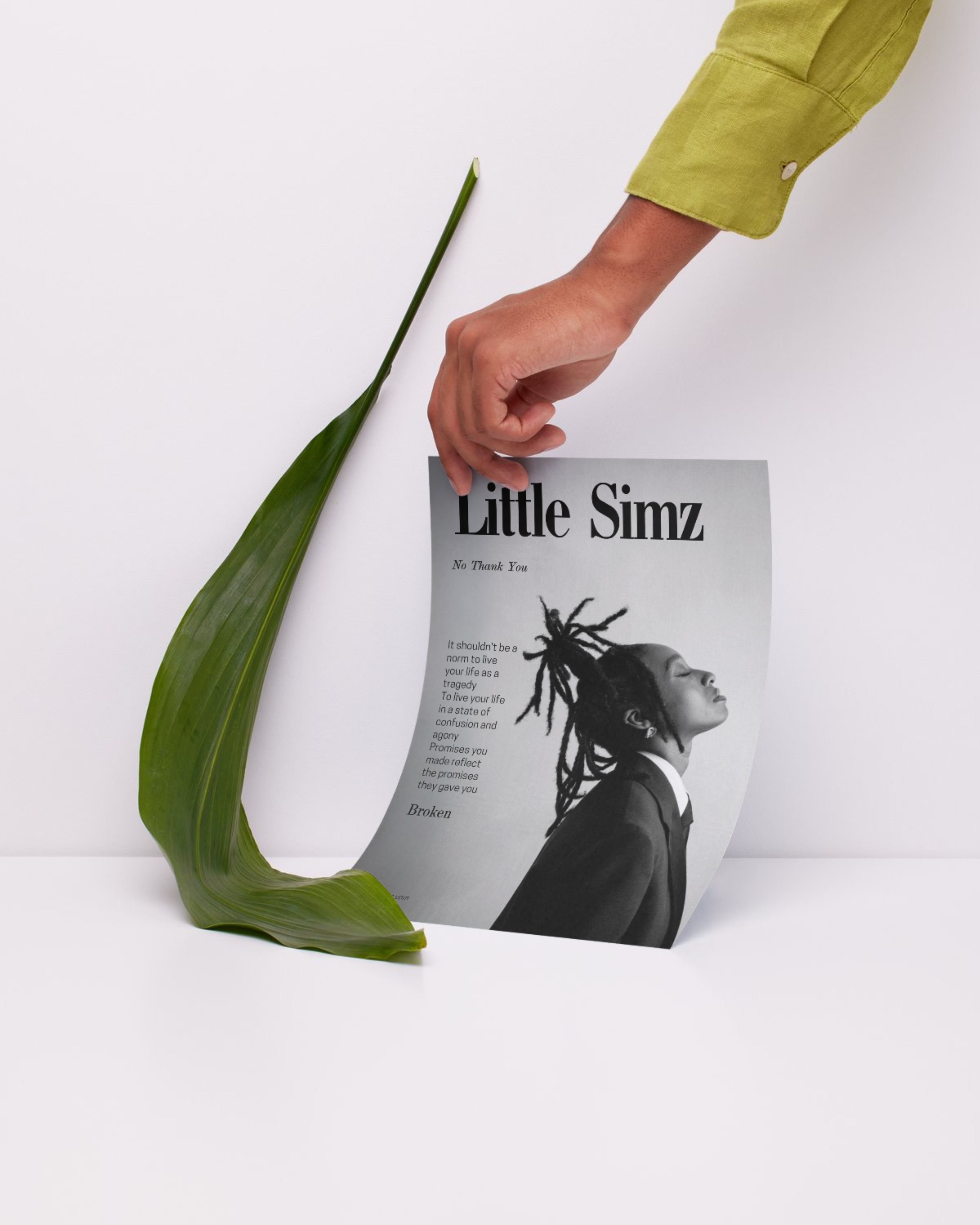 a hand holding a poster against a wall. a black and white poster with photo of little simz and in the side there is quote written by her - "It shouldn't be a norm to live your life as a tragedy.."